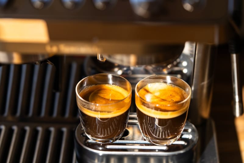 Two freshly pulled espressos under a machine, golden crema visible