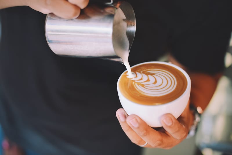 Barista pouring milk to create latte art in a cappuccino cup