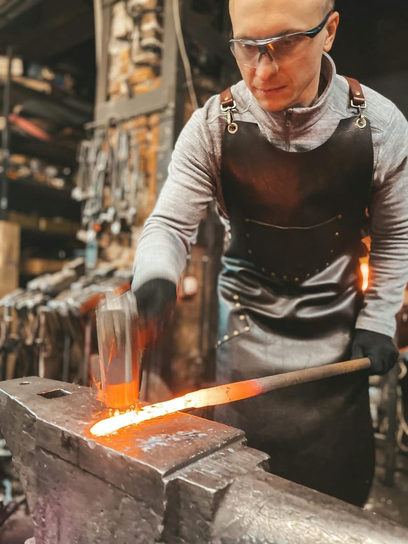Blacksmith in leather apron hammering glowing steel